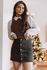 woman wearing a brown ribbed knit vest over a white blouse and a black button-up denim mini skirt