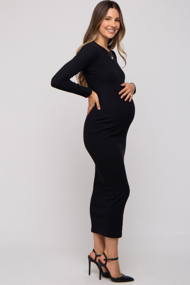 woman wearing a black long sleeve maternity dress, showing her baby bump and smiling while standing sideways