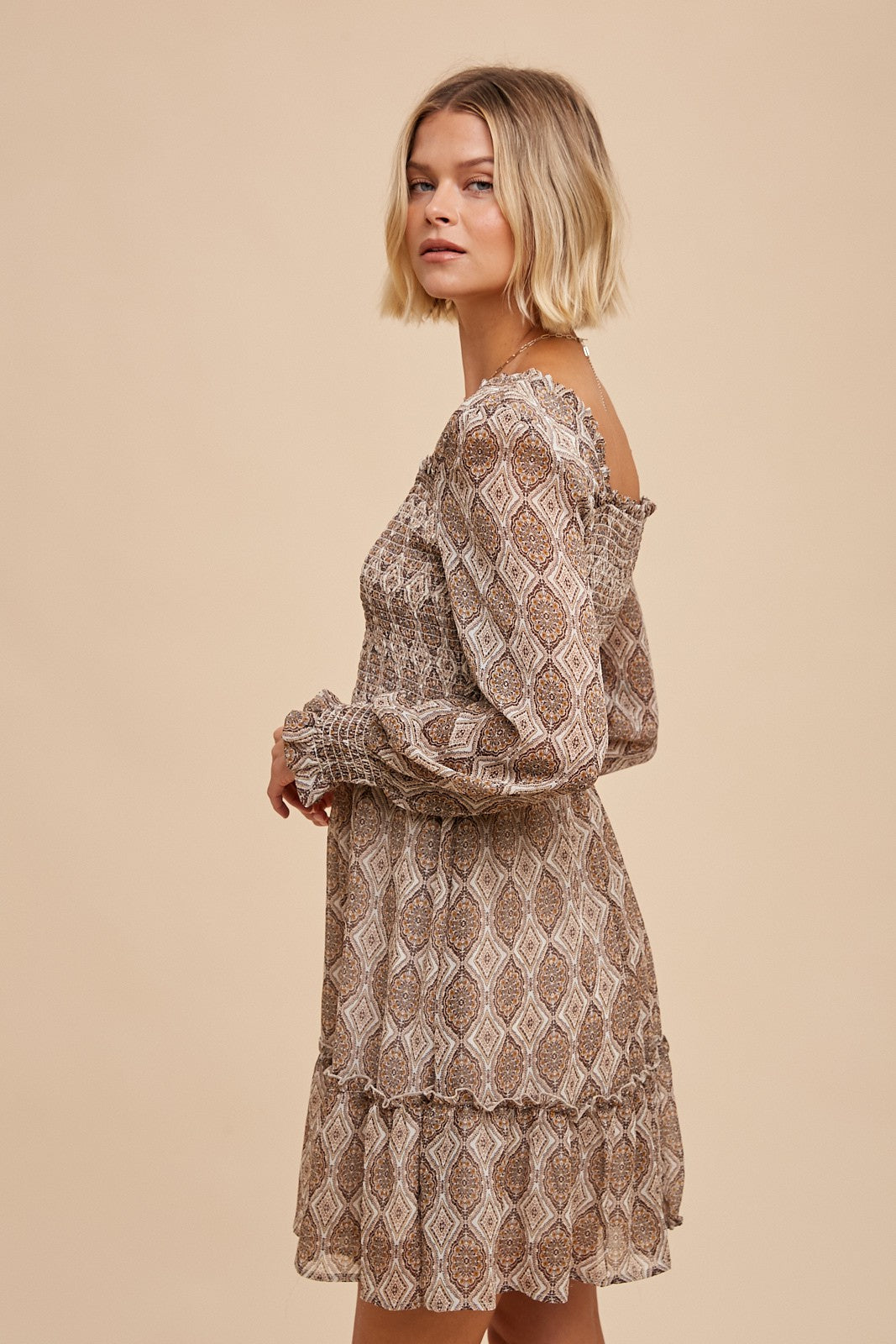 woman wearing a brown patterned mini dress with long sleeves and ruffle hem detailing