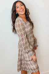 woman wearing a brown patterned long sleeve dress with a fitted bodice and flowy skirt, smiling at the camera
