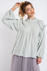woman wearing a light green long sleeve ruffled blouse with pleating detail and puff sleeves, paired with a tulle skirt