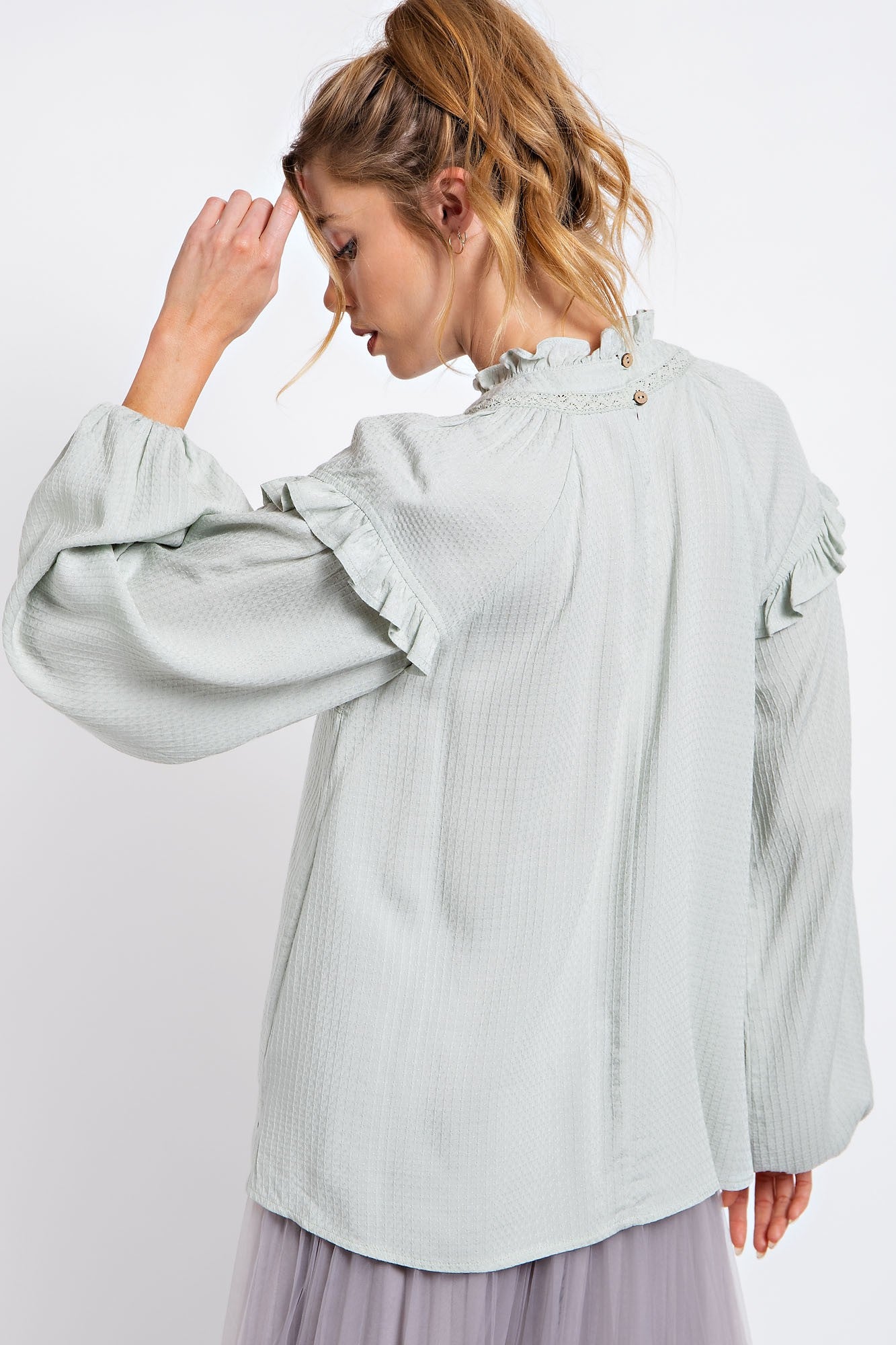 woman wearing a light green long sleeve blouse with ruffled detailing and a button closure at the back