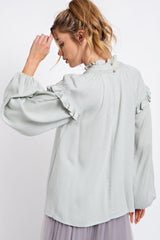 woman wearing a light green long sleeve blouse with ruffled detailing and a button closure at the back