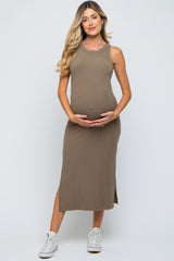 woman wearing a khaki sleeveless maternity dress, holding her baby bump and standing in white sneakers