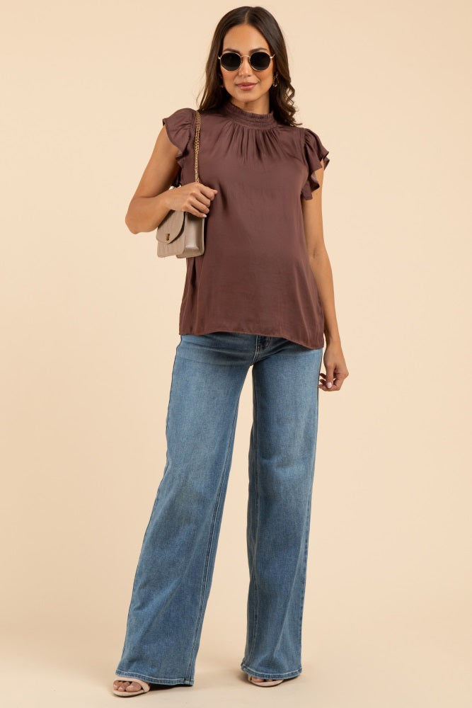 woman wearing a brown maternity top with ruffled sleeves and blue wide-leg jeans, accessorized with sunglasses and a shoulder bag