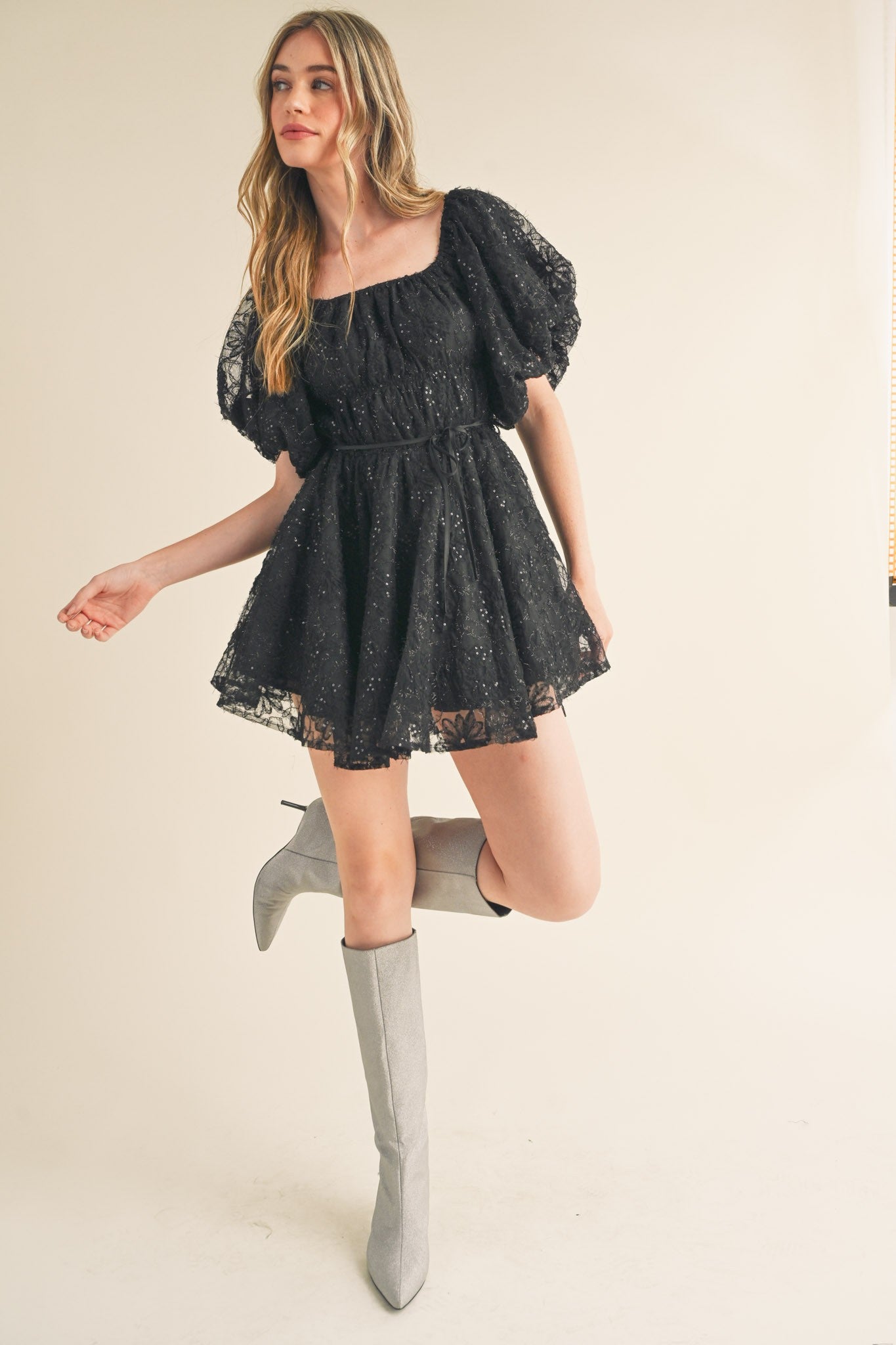 woman wearing a black lace puff sleeve dress with a fitted waist and loose skirt, paired with gray knee-high boots
