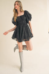 woman wearing a black lace puff sleeve dress with a fitted waist and loose skirt, paired with gray knee-high boots