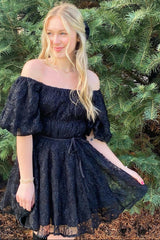 woman wearing a black off-the-shoulder puff sleeve dress with a cinched waist and lace detailing in an outdoor setting