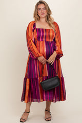 woman wearing a colorful striped maternity plus dress with long sleeves and a tiered hem, holding a black handbag