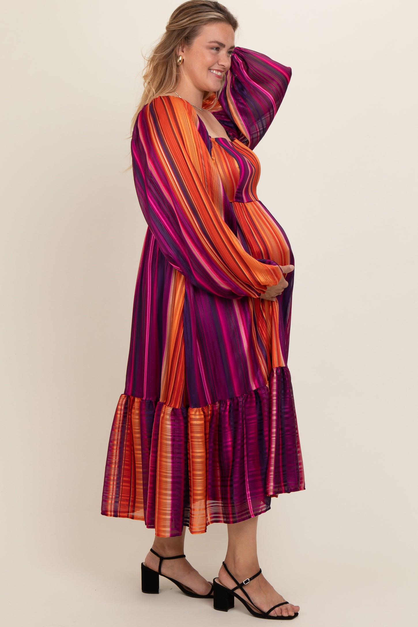 woman wearing a multicolored striped maternity dress with long sleeves and a ruffled hem, holding her baby bump