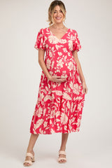 woman wearing a pink floral maternity dress with a v-neck and tiered skirt, holding her baby bump