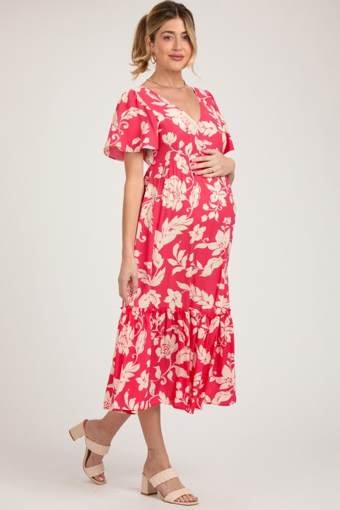 woman wearing a pink floral maternity dress with ruffled hem and holding her baby bump