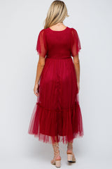 woman wearing a burgundy maternity dress with sheer sleeves and a tiered tulle skirt, showing a baby bump from the back