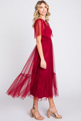 woman wearing a burgundy tulle maxi dress with short sleeves and a ruffled hem, styled with nude heels