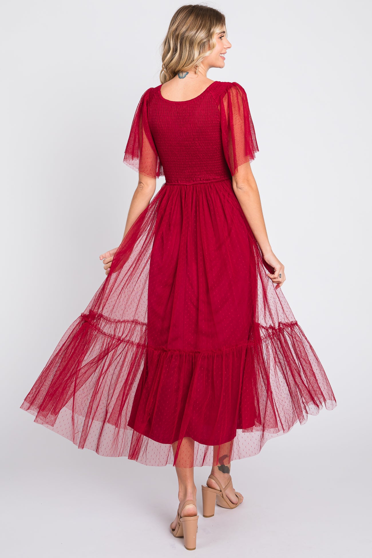 woman wearing a red maxi dress with tulle sleeves and a tiered skirt, showing the back view.