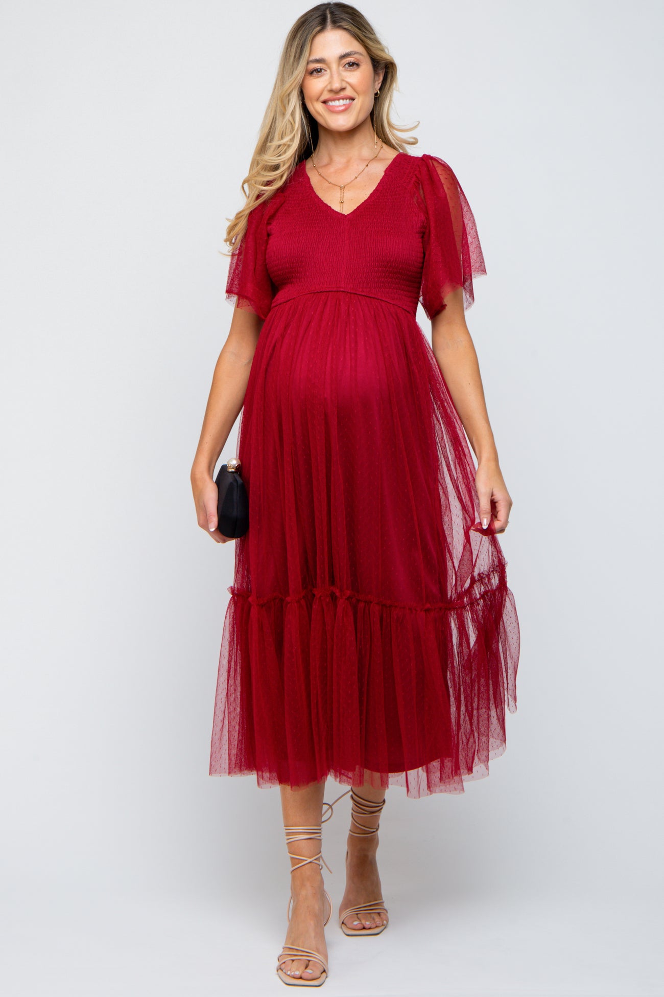 woman wearing a red maternity dress with ruffle sleeves and a layered tulle skirt, showcasing her baby bump