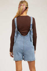 woman wearing a brown long sleeve top and denim maternity overalls, with a baby bump visible