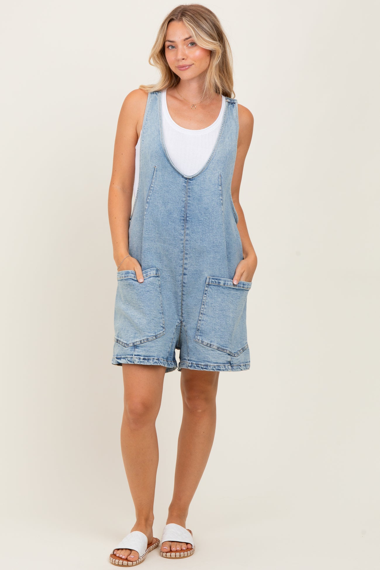 woman wearing a light blue denim overall romper with front pockets and a white tank top underneath