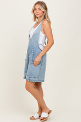 woman wearing a light wash denim overall dress with front pockets over a white tank top and styled with white sandals