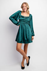 woman wearing a dark teal long sleeve mini dress with gathered front and a square neckline