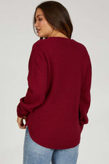 woman wearing a deep burgundy oversized knitted maternity sweater with long sleeves and side slits, viewed from the back