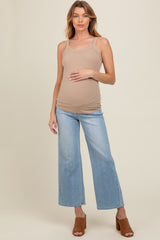 woman wearing a beige ribbed maternity tank top and blue wide-leg jeans, holding her baby bump