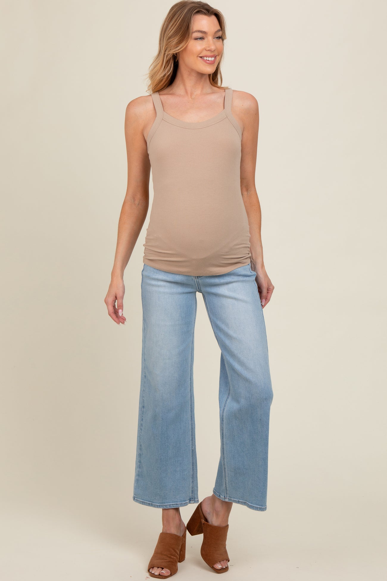 woman wearing a beige maternity tank top and light blue wide-leg jeans, showing a baby bump