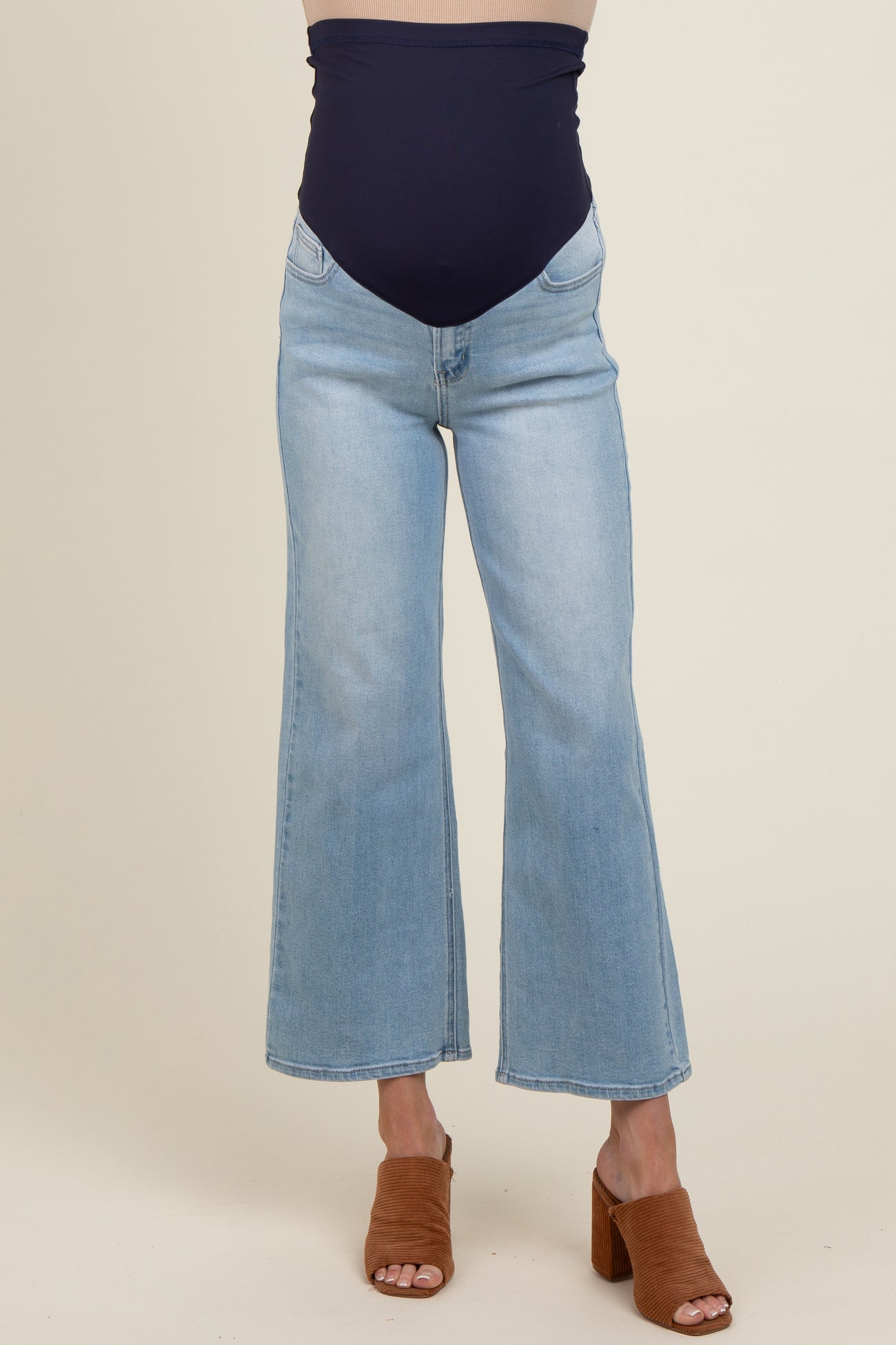 woman wearing a maternity light blue flared jeans with a navy blue belly band and brown heeled mules