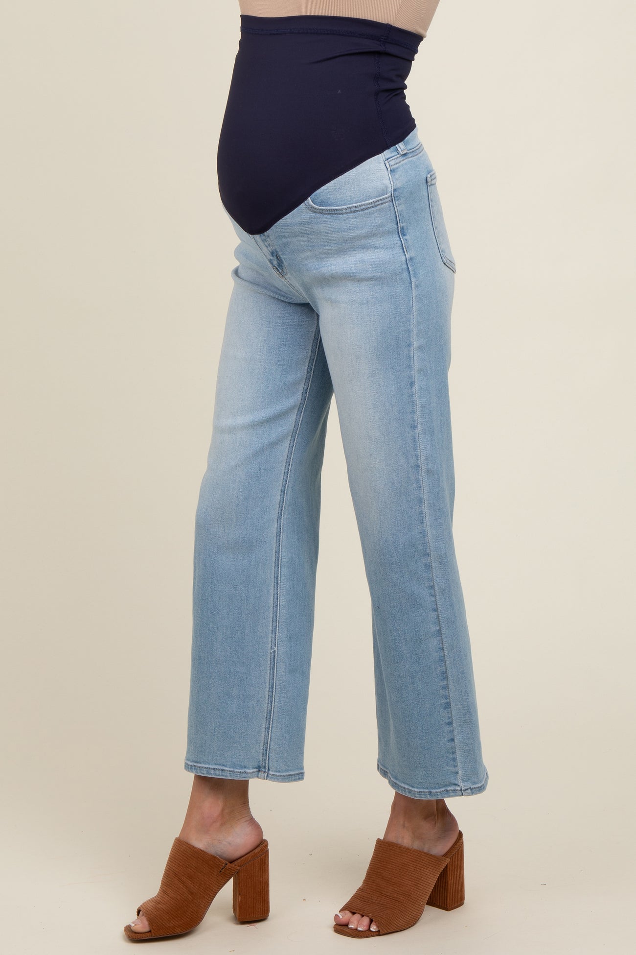 woman wearing light blue maternity jeans with a stretchy dark blue waistband and heeled sandals, showing a baby bump