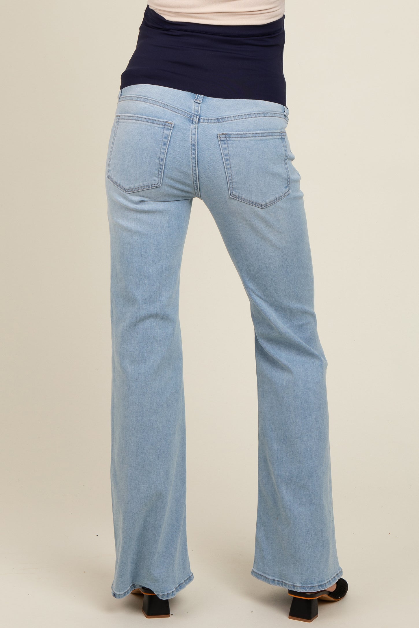 woman wearing light blue maternity jeans with a wide flare, showing the back view and a stylish waistband design