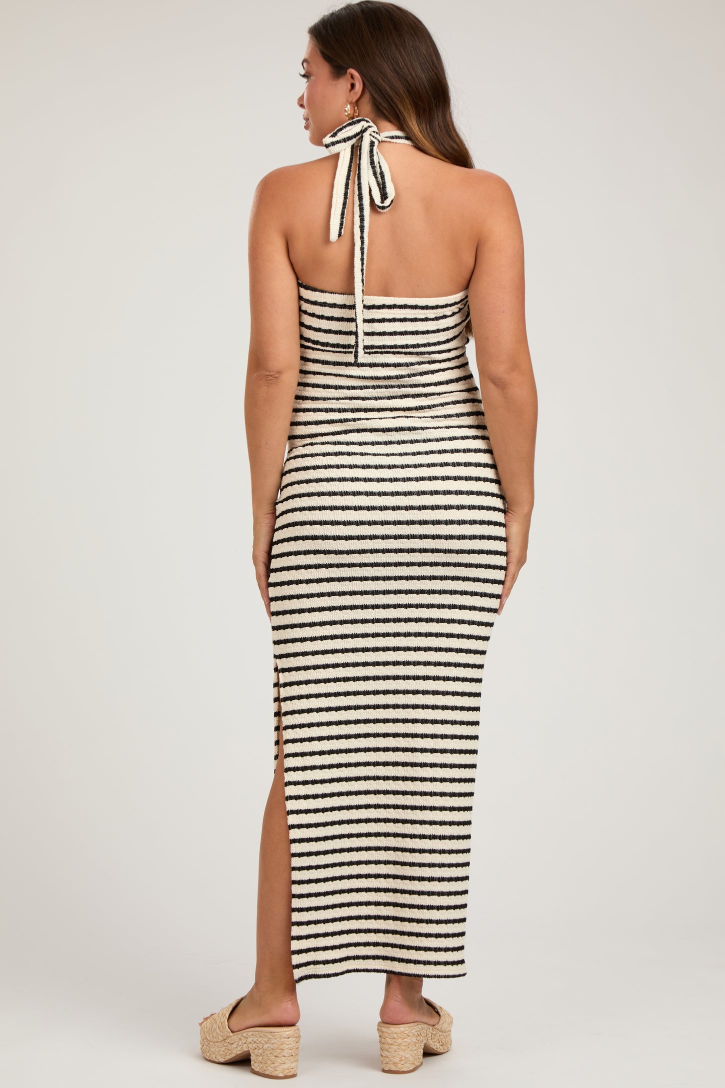 woman wearing a black and white striped maternity maxi dress with a halter neck and side slit
