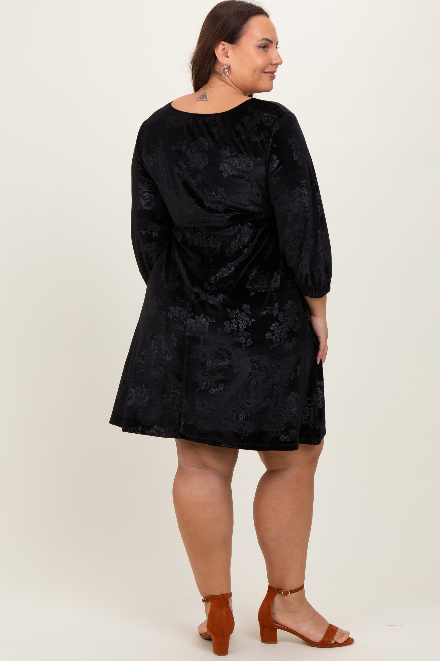 woman wearing a black floral printed plus size dress with three-quarter sleeves and a flared silhouette, viewed from the back