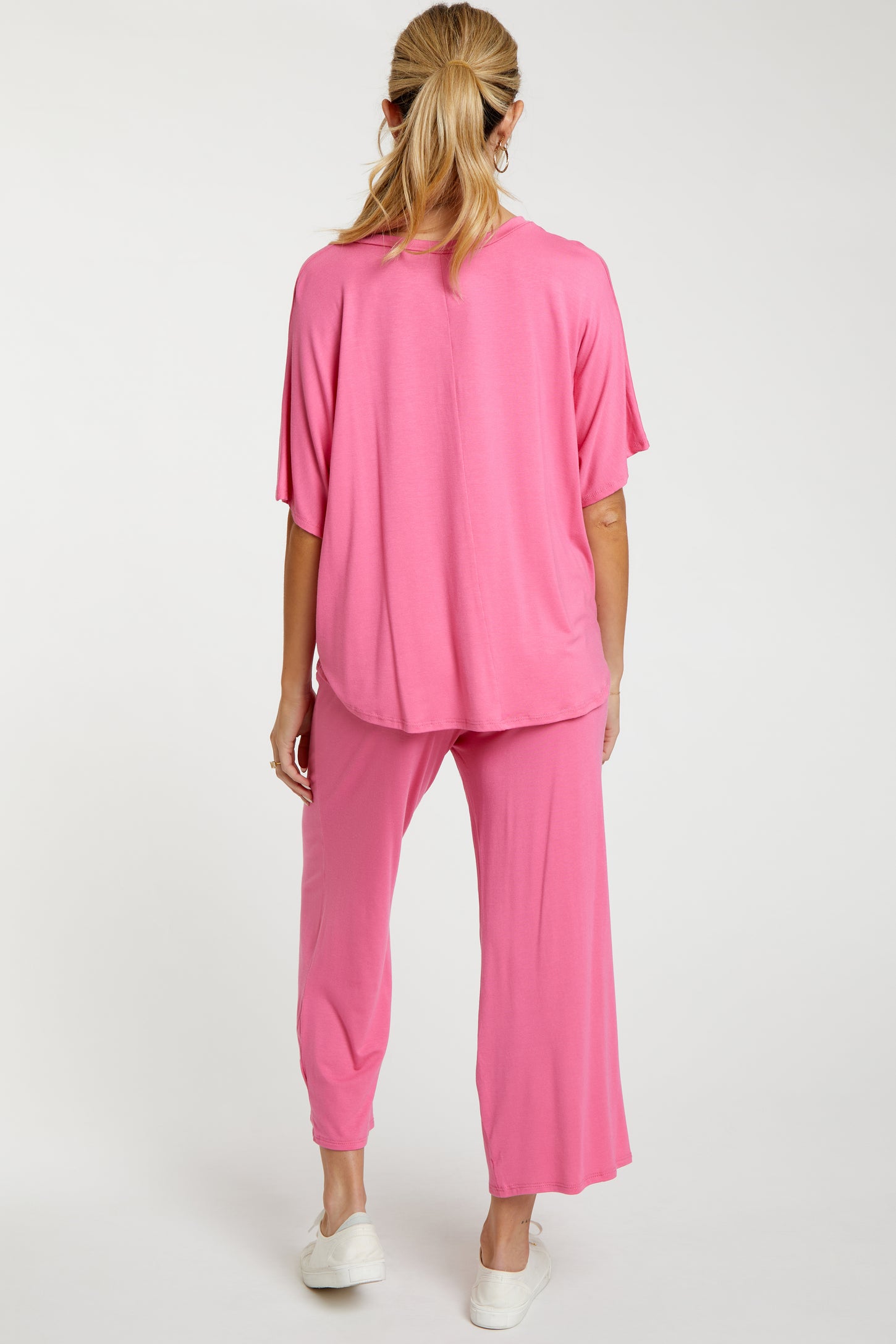 woman wearing a pink maternity loungewear set consisting of a loose top and cropped pants, showing her back