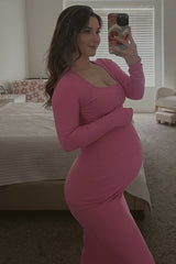 woman wearing a pink long sleeve maternity dress showing her baby bump while taking a selfie in a mirror