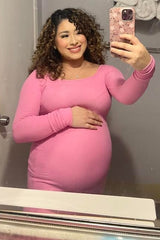 woman wearing a fitted pink long sleeve maternity dress with her baby bump visible, taking a selfie in the mirror