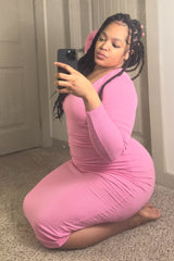 woman wearing a pink long sleeve fitted dress, posing while kneeling and taking a selfie in front of a mirror