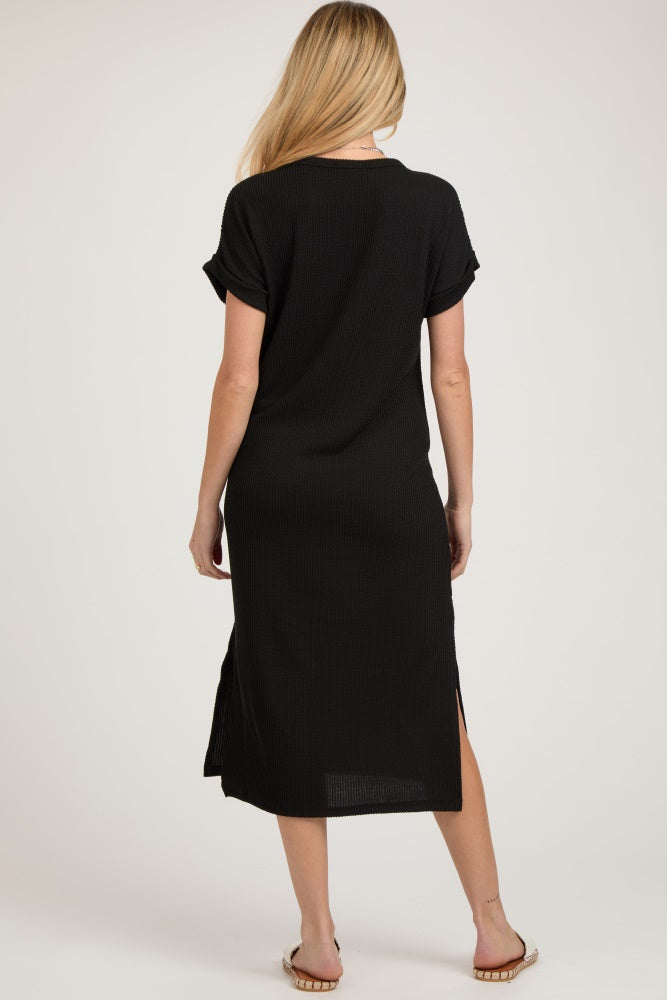 woman wearing a black maternity maxi dress with short rolled sleeves and side slits, showing a pregnancy belly