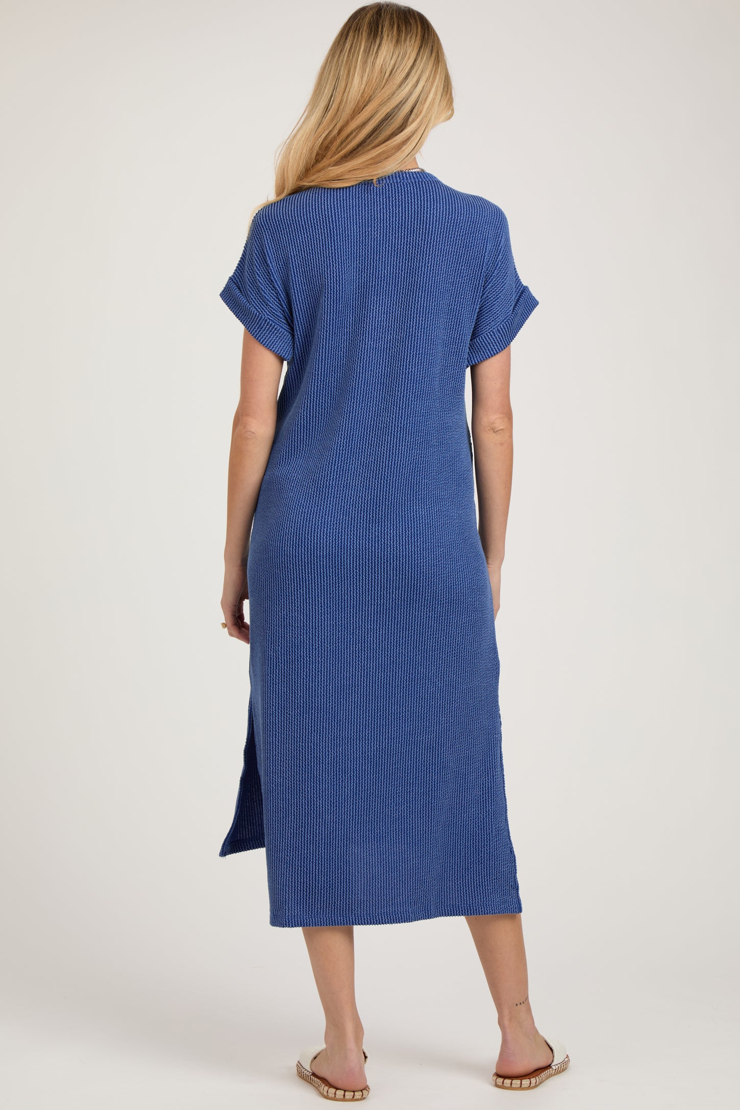 woman wearing a long blue striped maternity dress with short sleeves and a knee-high side slit seen from the back