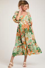 woman wearing a green and orange floral maternity dress with puff sleeves and a smocked bodice, showcasing her baby bump