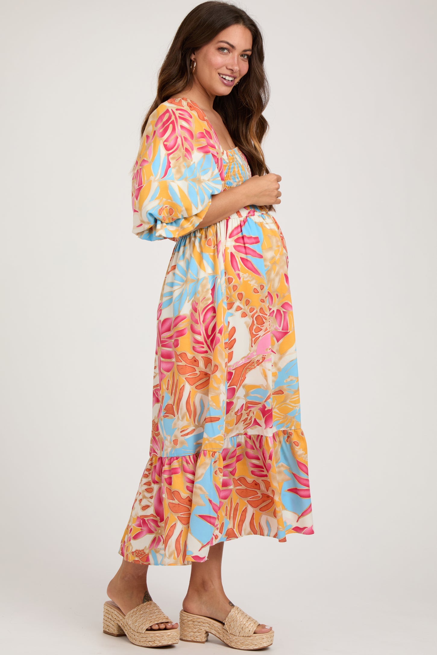 woman wearing a colorful floral maternity maxi dress with short puff sleeves and holding her baby bump