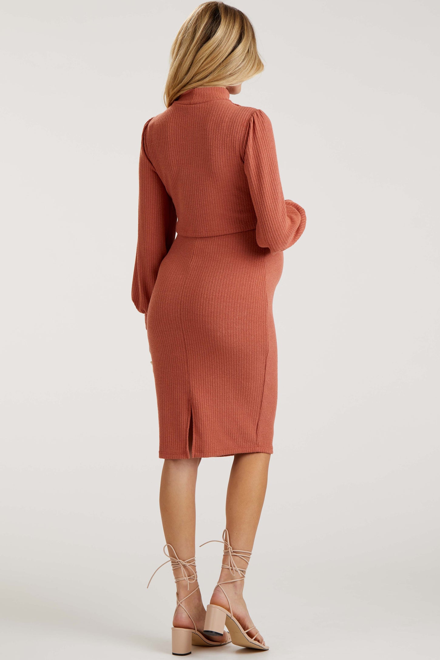 woman wearing a rust ribbed knit maternity dress with long sleeves and a side slit, showcasing her baby bump