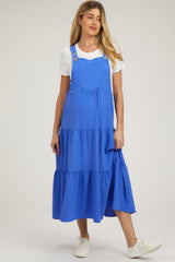 woman wearing a bright blue maternity dress with adjustable straps and tiered ruffle details over a white t-shirt