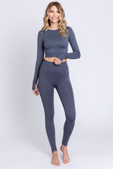 woman wearing a navy long sleeve crop top and matching high-waisted leggings, standing barefoot against a white background