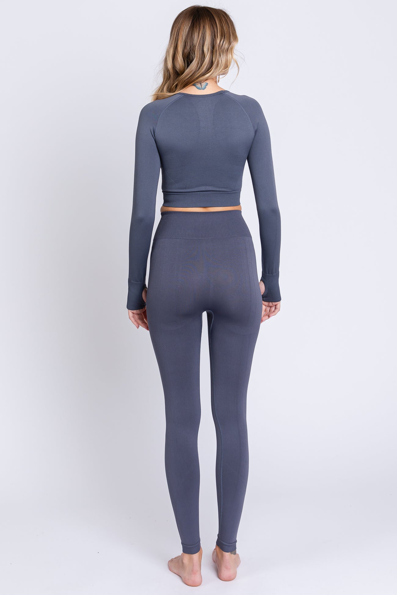woman wearing a gray long sleeve crop top and matching high-waisted leggings, viewed from the back