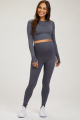 woman wearing a gray long sleeve maternity crop top and matching maternity leggings, smiling and standing in a relaxed pose