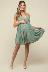 woman wearing a sage green maternity dress with spaghetti straps and a flowing skirt, holding her baby bump