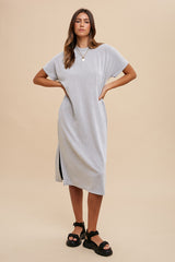 woman wearing a grey ribbed midi dress with short sleeves and side slits, standing against a neutral background
