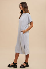 woman wearing a light gray casual midi dress with short sleeves and side pockets, styled with black sandals