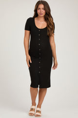 woman wearing a black ribbed maternity dress with short sleeves and button detailing, showcasing a baby bump