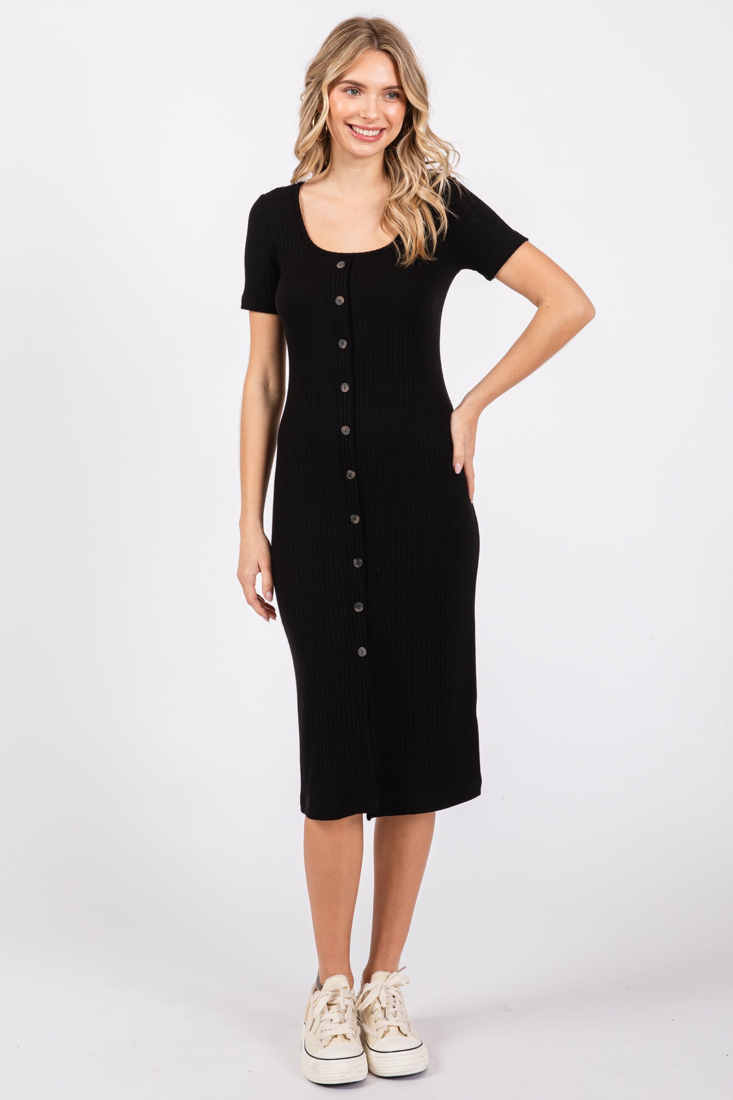 woman wearing a black ribbed midi dress with short sleeves and button detailing, paired with sneakers